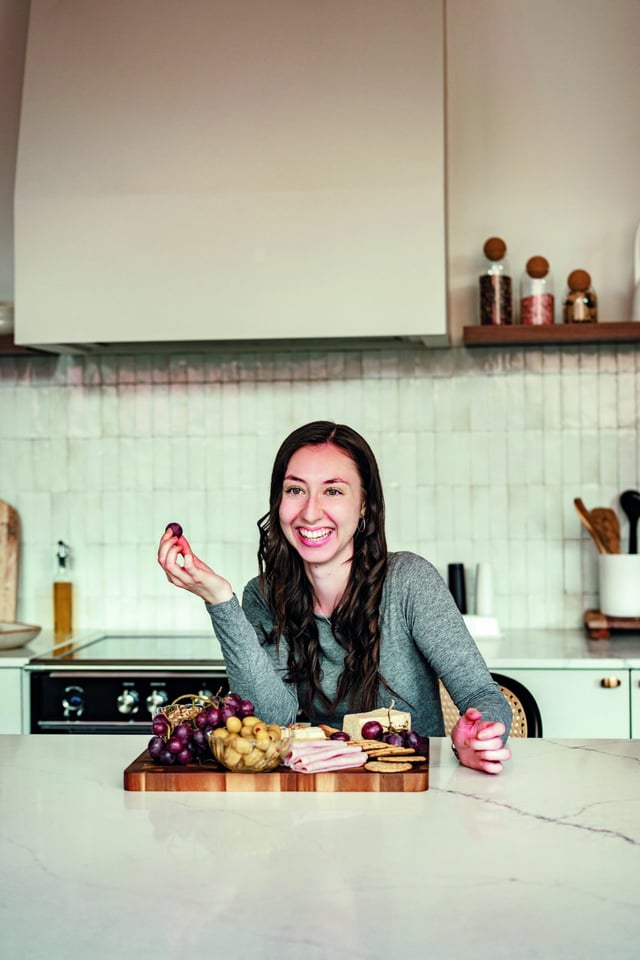 Emilie rit, attablée devant une planche de fromages